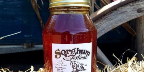 A jar of sorghum syrup labeled "Sorghum Festival," resting on straw with a rustic background.