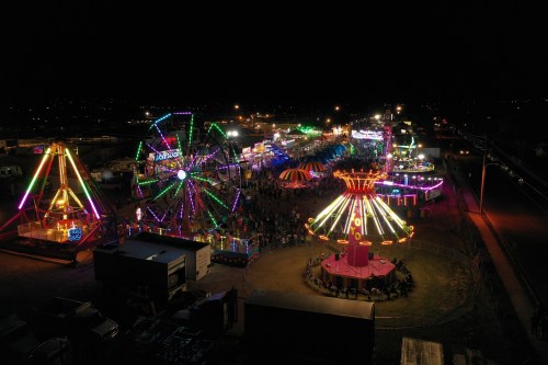 Aerial view of a vibrant night fair with colorful lights, rides, and crowds enjoying the festivities.