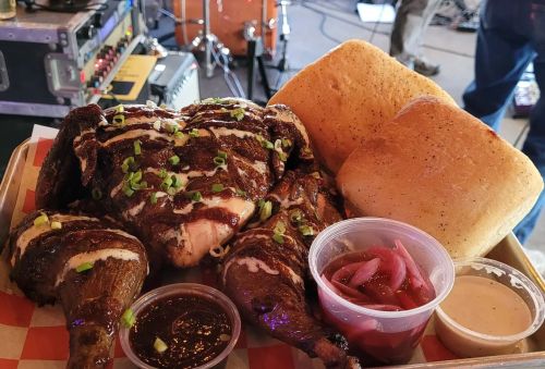 A platter of seasoned grilled chicken with sauces, pickled onions, and two pieces of bread, set against a music backdrop.
