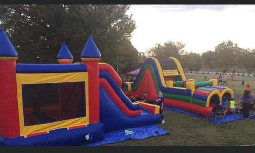 Colorful inflatable bounce house and slide set up in a grassy area, with people enjoying the outdoor event.