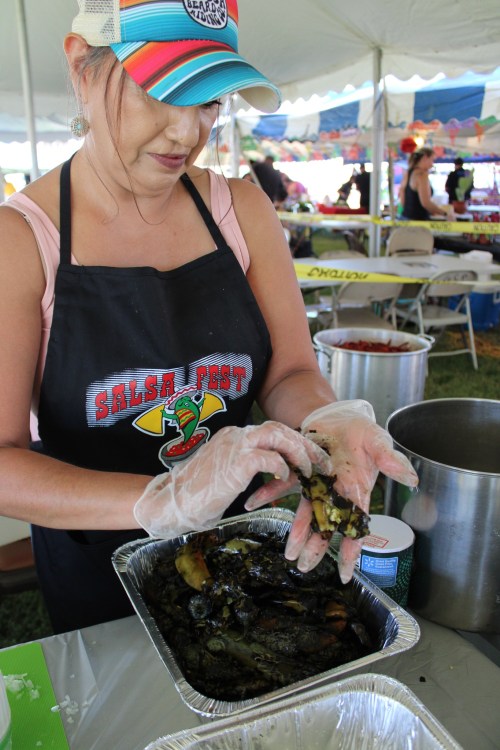 A woman in an apron prepares food at a festival, wearing gloves and handling ingredients in a tray.