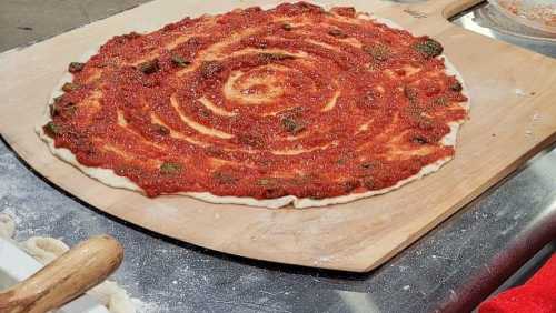 A pizza dough topped with a spiral of tomato sauce on a wooden pizza peel, ready for baking.