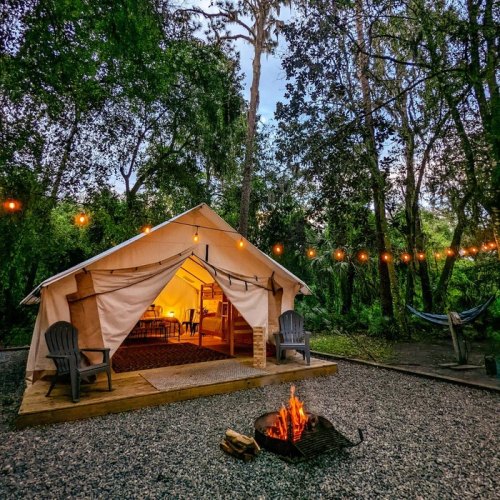 A cozy tent with a fire pit outside, surrounded by trees and string lights, creating a warm, inviting atmosphere.