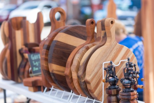 A display of wooden cutting boards and pepper mills at a market, showcasing various shapes and wood grains.