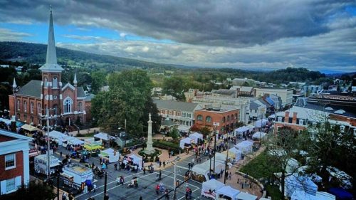 Aerial view of a town square with a church, vendors, and people enjoying a festival under a cloudy sky.