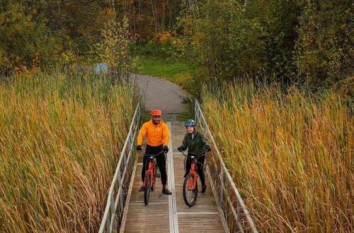 Two cyclists on a wooden bridge surrounded by tall grass and trees, enjoying a fall day outdoors.