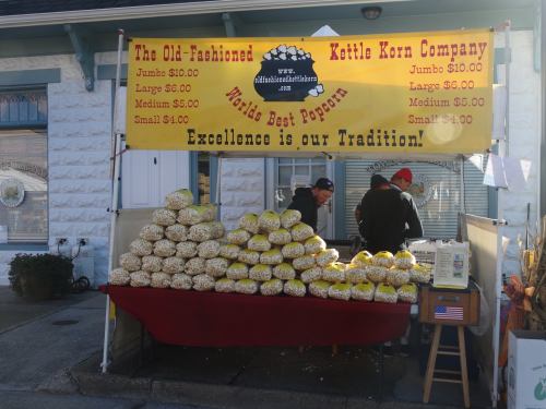 A popcorn stand with bags of kettle corn for sale, featuring a sign that reads "World's Best Popcorn" and prices listed.