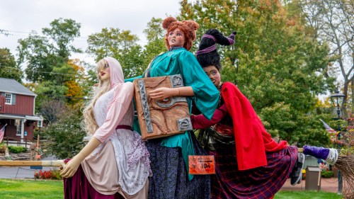 Three whimsical Halloween mannequins dressed as witches, surrounded by autumn foliage and festive decorations.