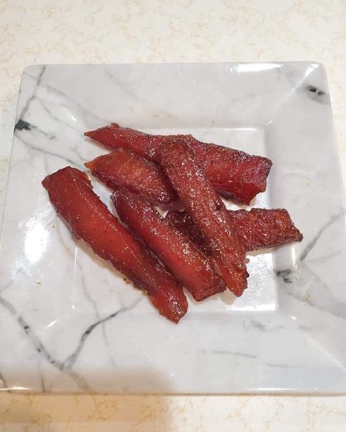 A plate of five pieces of shiny, reddish-brown cooked meat arranged on a marble-patterned dish.