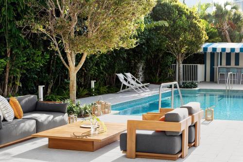 A modern outdoor space featuring a pool, lounge seating, and a striped cabana surrounded by lush greenery.