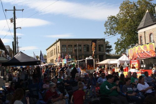 A lively street festival with crowds, food stalls, and colorful tents under a clear blue sky.