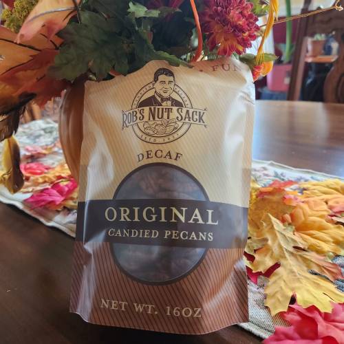 A bag of "Rob's Nut Sack" decaf original candied pecans on a table with autumn decorations.