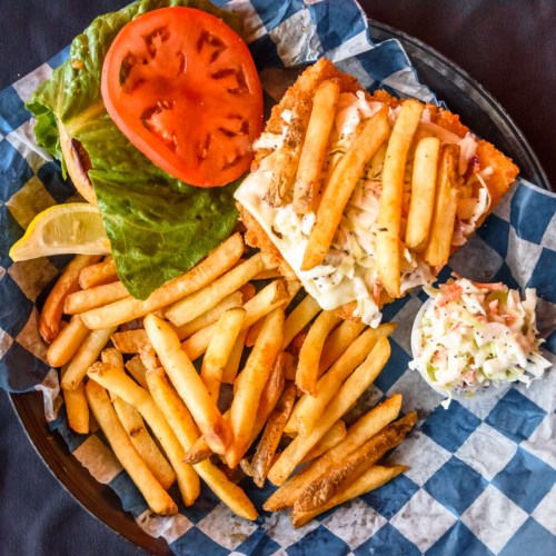 A plate featuring a sandwich with lettuce, tomato, and fries, accompanied by a side of coleslaw on a checkered paper.