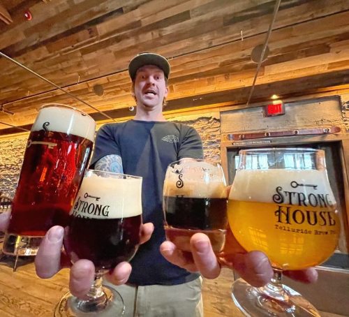 A person holds four glasses of beer, showcasing different colors and styles, in a rustic bar setting.