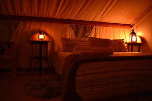 Cozy tent interior with a bed, soft lighting from lanterns, and towels neatly arranged on the bed.