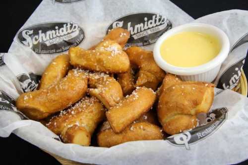 A basket of golden-brown pretzel bites sprinkled with salt, served with a side of cheese dip.