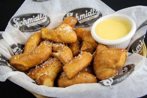 A basket of golden-brown pretzel bites sprinkled with salt, served with a side of cheese dip.