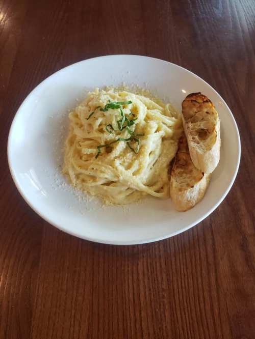 A plate of creamy pasta topped with herbs and served with a slice of toasted bread on the side.