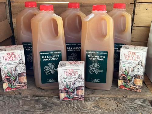 Bottles of apple cider and spice packets displayed on a wooden surface.