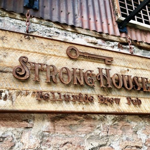 Sign for Strong House Telluride Brew Pub, featuring a key design and rustic wooden texture.