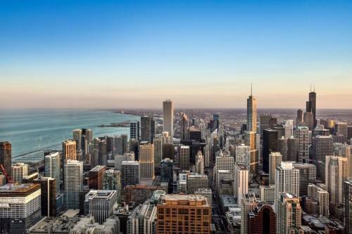A panoramic view of a city skyline with tall buildings and a lake in the background under a clear blue sky.