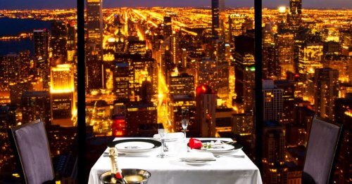 Elegant dining table set for two with a city skyline view at night, featuring sparkling lights and a romantic atmosphere.