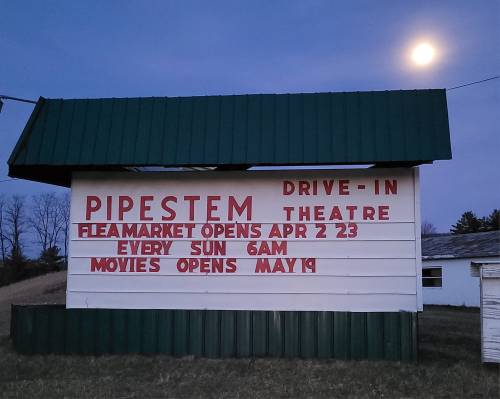 Sign for Pipestem Drive-In Theatre announcing flea market opening April 2, 2023, and movies starting May 19, with a full moon.