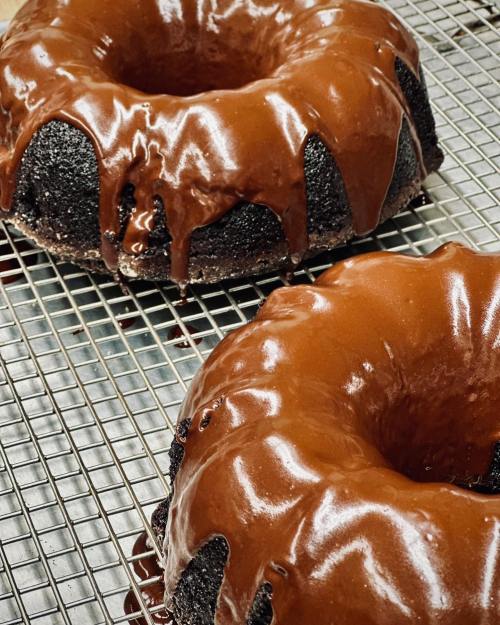 Two chocolate bundt cakes with glossy chocolate glaze, cooling on a wire rack.