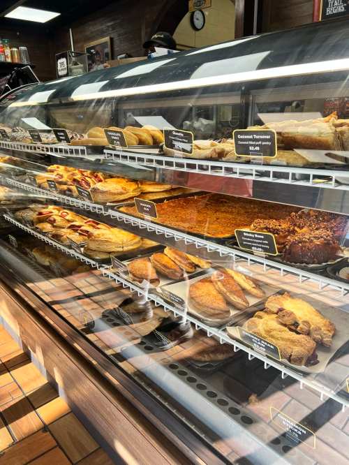A display case filled with various baked goods, including pastries, cookies, and desserts, in a bakery setting.
