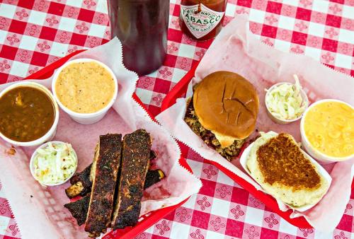 A spread of barbecue ribs, a sandwich, coleslaw, mac and cheese, and baked beans on a checkered tablecloth.