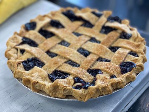 A freshly baked lattice-top pie filled with dark fruit filling, resting on a silver pie dish.
