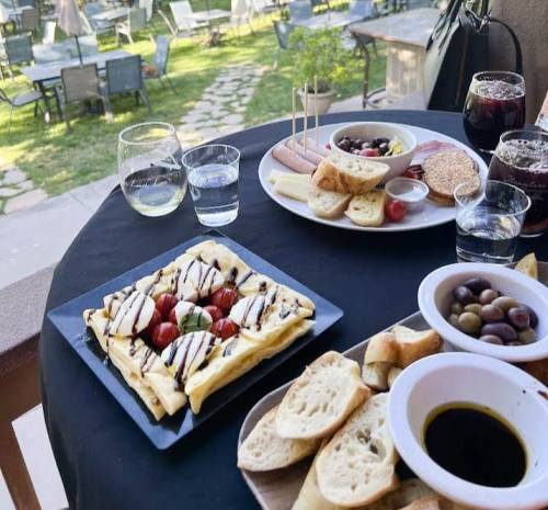 A table set with a variety of dishes, including a flatbread with tomatoes, olives, cheese, and drinks, in a garden setting.