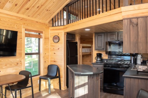 Cozy interior of a tiny home featuring wooden walls, a kitchen area, dining table, and a lofted sleeping space.