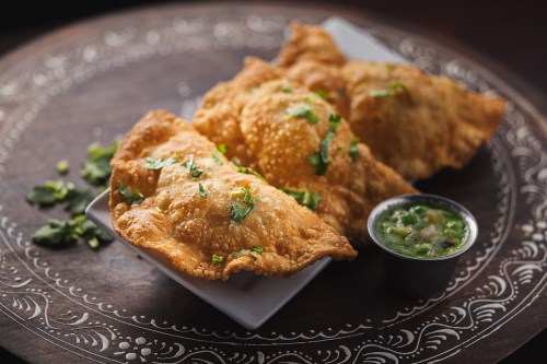 Three golden-brown samosas garnished with cilantro, served on a plate with a small bowl of green chutney.