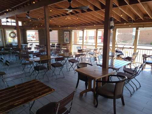 A spacious, empty dining area with wooden tables and chairs, featuring large windows and a wooden ceiling.