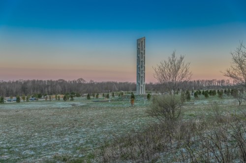 A tall tower stands in a snowy field at dusk, surrounded by trees and a clear sky transitioning to twilight.