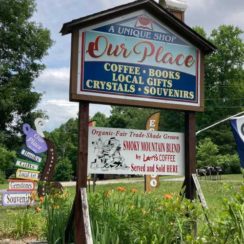 Sign for "Our Place" shop featuring coffee, books, local gifts, crystals, and souvenirs, with additional signs nearby.