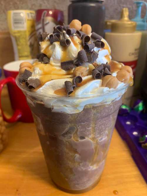 A delicious chocolate dessert drink topped with whipped cream, chocolate shavings, and caramel drizzle in a clear cup.