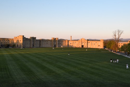 A large grassy field in front of a historic building at sunset, with people playing in the distance.
