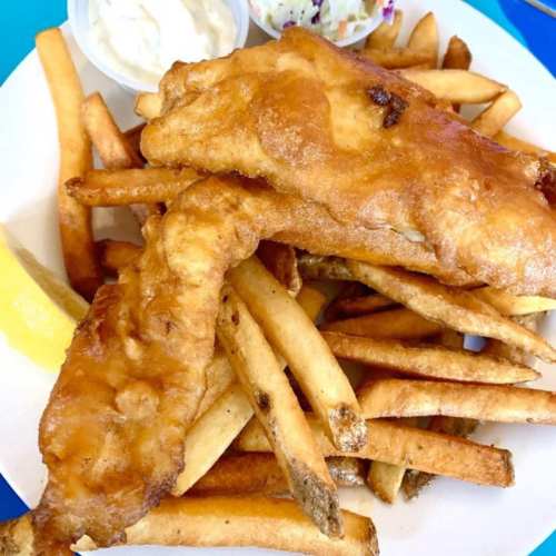 A plate of golden-brown fried fish fillets served with crispy French fries and a side of coleslaw and dipping sauce.