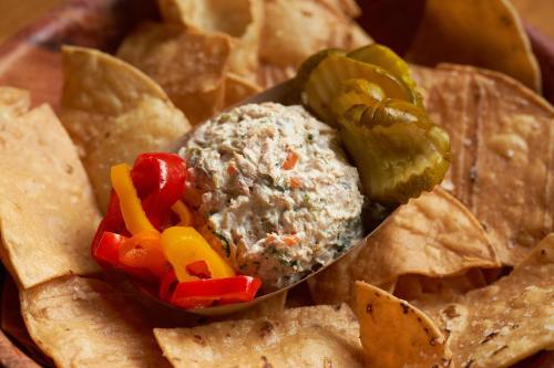 A bowl of creamy dip surrounded by tortilla chips, garnished with sliced peppers and pickles.