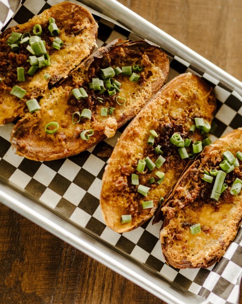 A tray of toasted bread topped with cheese, meat, and chopped green onions, served on a checkered paper.
