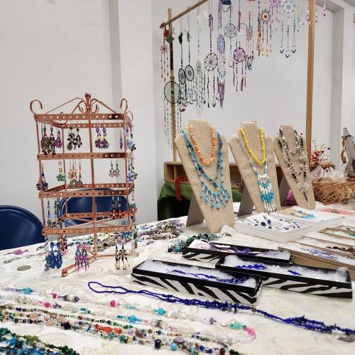 A display of colorful handmade jewelry, including earrings and necklaces, on a table with decorative stands.