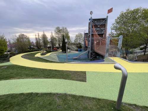 A colorful playground with winding paths, a climbing structure, and trees under a cloudy sky.