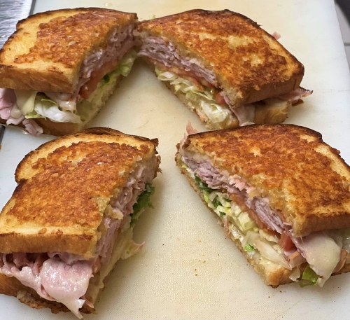 A toasted sandwich cut into quarters, filled with layers of ham, lettuce, tomato, and cheese.