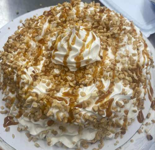 A round cake topped with whipped cream, chopped nuts, and caramel drizzle.