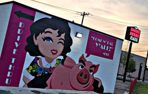 Colorful mural featuring a woman and a pig, with a "Drive Thru" sign and the phrase "Come 'n eat, y'all!"