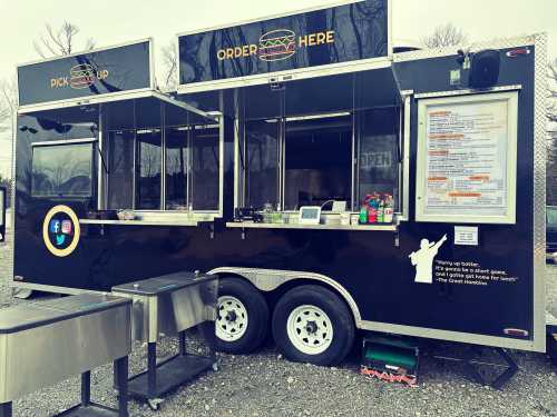 A food truck with a black exterior, featuring windows for ordering and a menu displayed on the side.