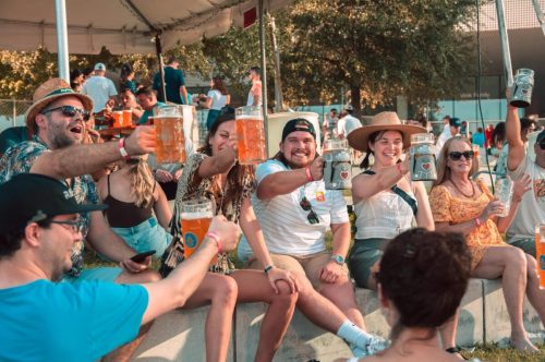 A group of people cheerfully raising large drinks at an outdoor gathering, enjoying a festive atmosphere.