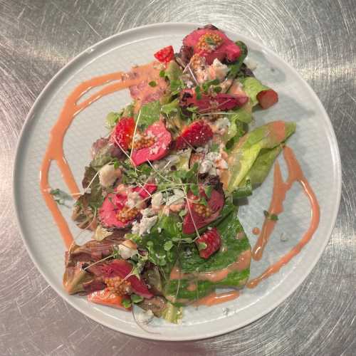 A vibrant salad with mixed greens, sliced beef, strawberries, and a creamy dressing, garnished with microgreens.